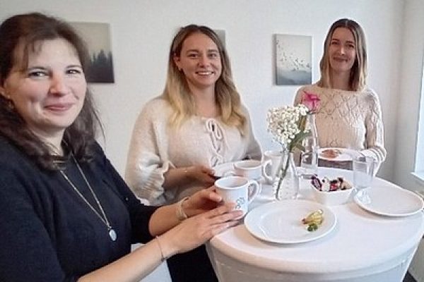 Mehrere Frauen stehen an einem Stehtisch und stoßen mit Getränken an